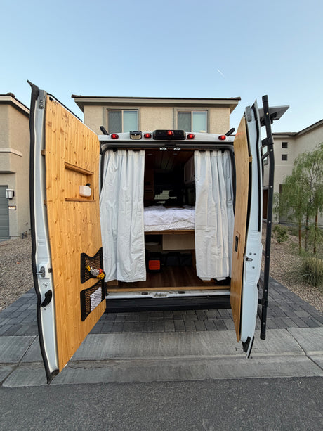 Custom rv rental interior visible through open rear doors, featuring a cozy bed, wood paneling, and practical storage for travel.
