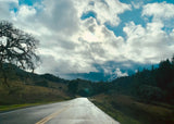 Winding road through green hills & mossy trees under a dramatic, cloudy sky. Perfect for an RV rental road trip!