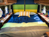 Cozy RV rental bedroom with colorful headboard, blue bedding, and berry-patterned curtains. Perfect for travel.