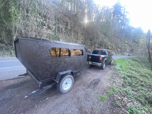 Black truck pulling a textured camper trailer on a scenic road. This compact RV rental is ready for outdoor adventures.
