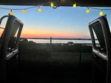 RV rental: Sunset over water, seen from open rear doors with warm string lights above.