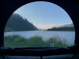 Inside your RV rental: a screened window reveals a tranquil lake, lush mountains, and clear skies, ideal for nature escapes.