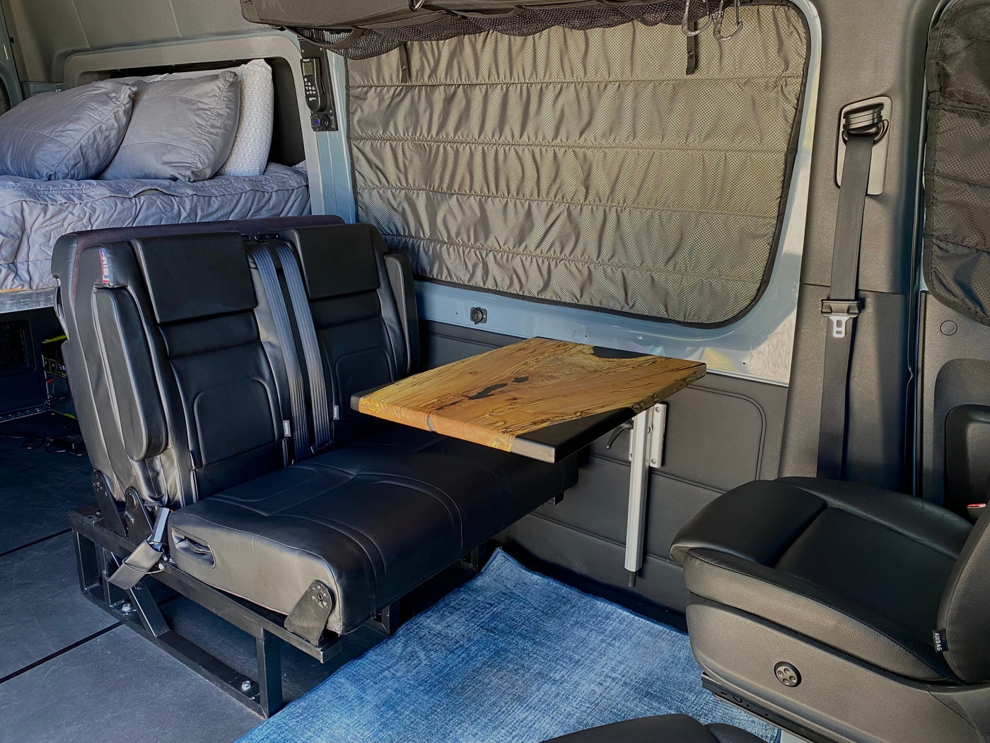 RV rental: Modern camper van interior with a cozy bed, comfortable seating area, and a natural wood table. — photo 9