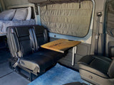 RV rental: Modern camper van interior with a cozy bed, comfortable seating area, and a natural wood table.