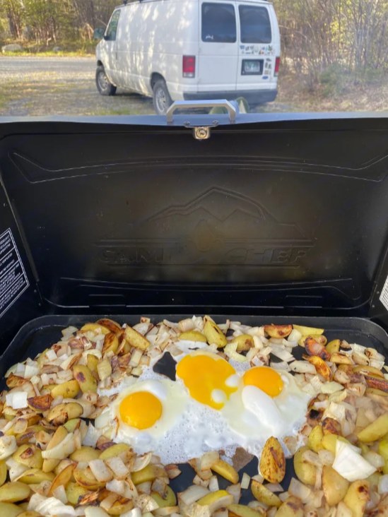 RV rental adventure! Cooking a hearty breakfast of eggs and potatoes on a portable griddle in a scenic outdoor setting.