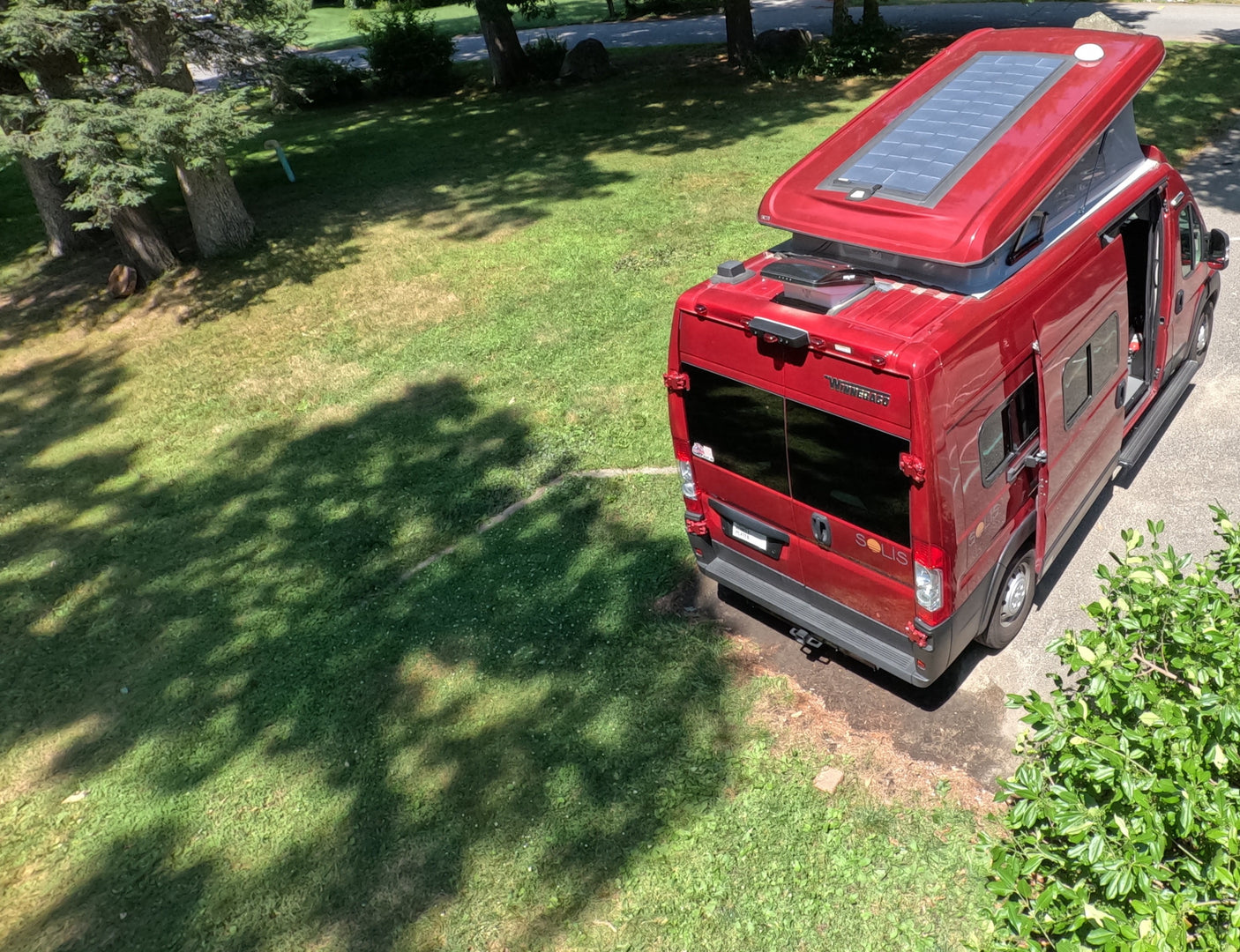 Red Winnebago Solis pop-top camper van with solar panels parked on pavement, ready for your RV rental journey.