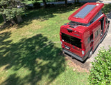 Red Winnebago Solis pop-top camper van with solar panels parked on pavement, ready for your RV rental journey.
