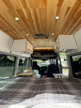 Interior of an RV rental with a wooden ceiling, recessed lights, plaid bed, and kitchen sink, looking towards the front cabin.
