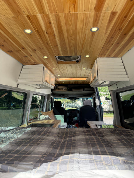Interior of an RV rental with a wooden ceiling, recessed lights, plaid bed, and kitchen sink, looking towards the front cabin.