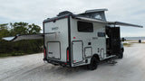 This modern Winnebago EKKO rv rental, with pop-top and extended awnings, is parked on sand near water, perfect for adventure.