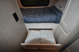 RV rental sleeping area showing a made bed and an open under-bed drawer with folded towels.