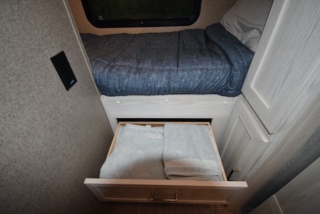 RV rental sleeping area showing a made bed and an open under-bed drawer with folded towels.