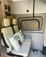 View of a modern RV rental interior featuring quilted seats, camping pillows, a control panel, and a palm tree window shade.