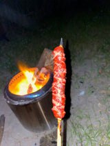 RV rental camping fun: Grilling a spiral-cut sausage over an outdoor fire pit at night. Classic campfire food for your trip!
