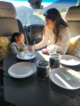 Mother and child enjoy a cheerful moment inside their RV rental, set with plates and mugs, ideal for family travel.