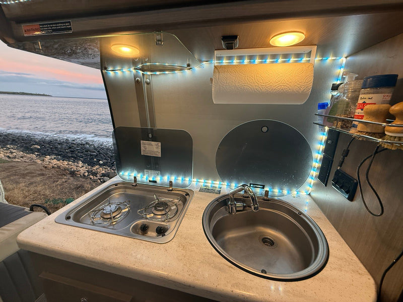 Inside an RV rental: compact kitchen with stove, sink, and glowing LED lights, framed by a serene ocean vista. — photo 16