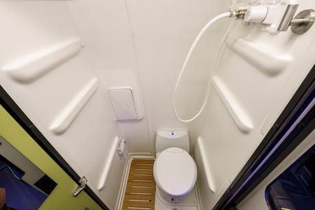 Compact white bathroom of an RV rental, featuring a toilet, shower, and wooden floor mat.