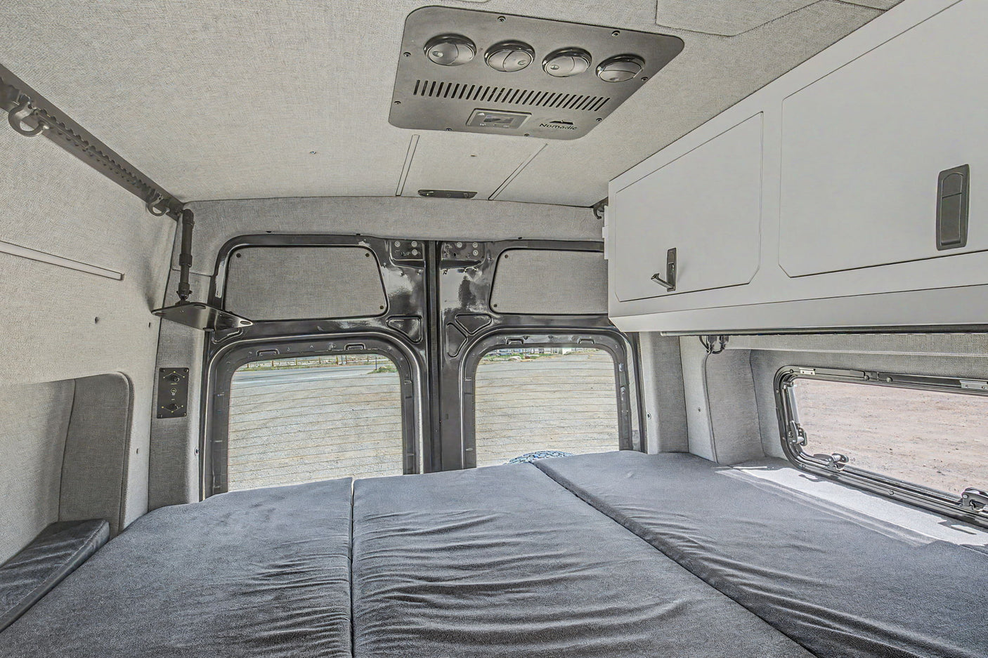 This RV rental interior features a cozy bed, overhead AC, and storage cabinets, ideal for comfortable camper van adventures.
