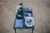 RV rental adventure essentials: a portable kitchen setup with stove, cookware, and utensils on a camping table for outdoor meals.