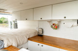 Bright RV rental interior with bed, white cabinets, wooden counter, and subway tile backsplash. Ready for your next adventure.