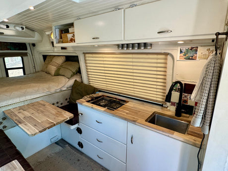 Compact RV rental interior: wood-countered kitchen with sink & stovetop, plus a comfy bed and smart storage solutions.