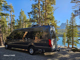 This luxurious Mercedes Sprinter RV rental is parked by a beautiful lake, surrounded by tall pine trees and mountains. Ideal for scenic adventures.
