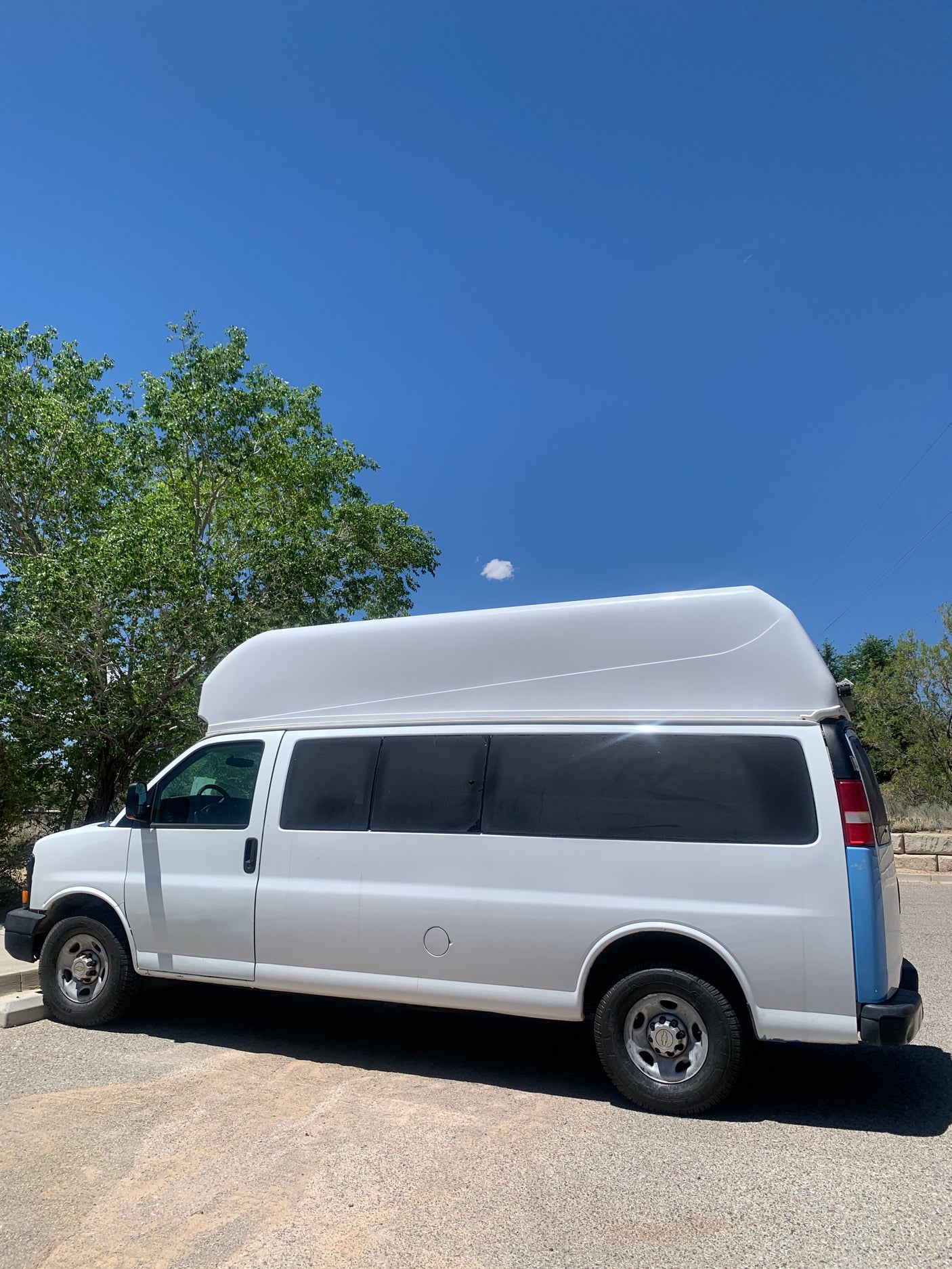 A white high-roof conversion van with a blue rear accent, ideal for an RV rental experience, parked under a clear sky.