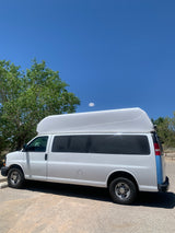 A white high-roof conversion van with a blue rear accent, ideal for an RV rental experience, parked under a clear sky.