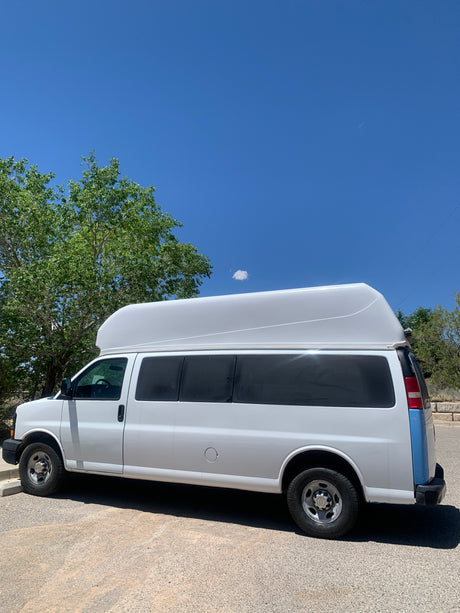 A white high-roof conversion van with a blue rear accent, ideal for an RV rental experience, parked under a clear sky.