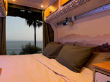 Relax in this cozy RV rental bed with an ocean view and ceiling-mounted projector, offering the ultimate van life experience.