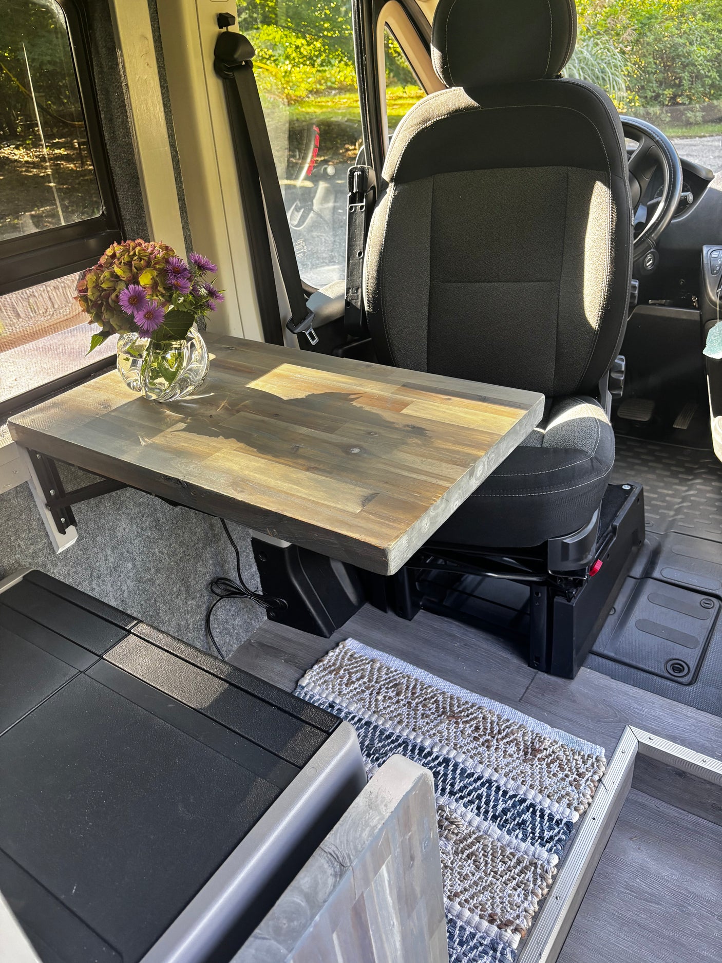 An RV rental's inviting interior: custom wooden table with flowers, vehicle seat, and storage unit. A compact travel space.