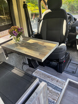 An RV rental's inviting interior: custom wooden table with flowers, vehicle seat, and storage unit. A compact travel space.
