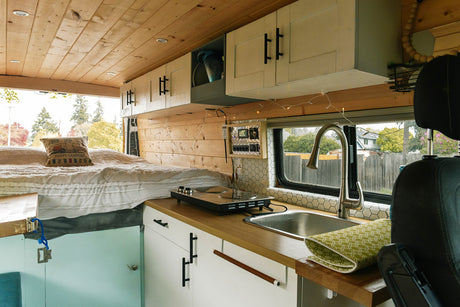 Cozy rv rental interior featuring a comfortable bed, compact kitchen with sink, stovetop, and wooden accents.