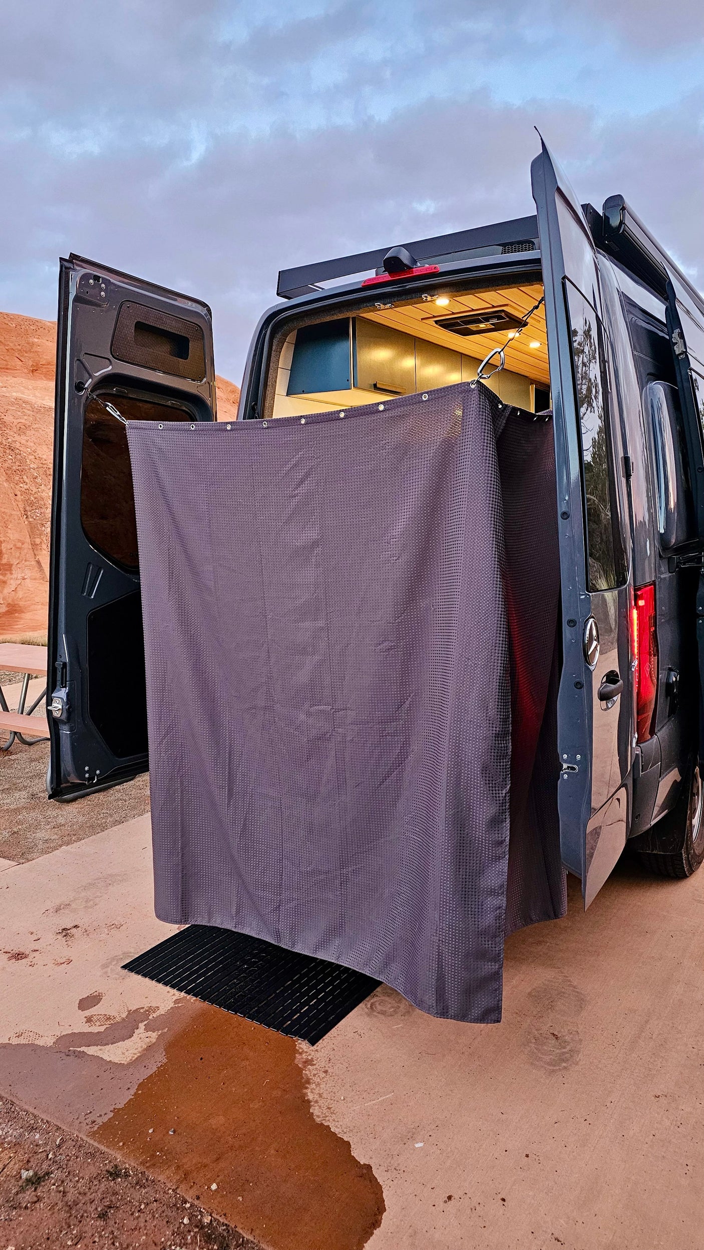 Enjoy convenience with this rv rental outdoor shower. A grey curtain creates a private space outside the camper van, with a mat catching water on the ground.
