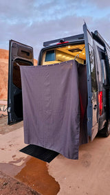 Enjoy convenience with this rv rental outdoor shower. A grey curtain creates a private space outside the camper van, with a mat catching water on the ground.