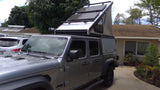 Silver Jeep Gladiator with pop-up camper & solar panels, ideal for rv rental or overlanding adventures.