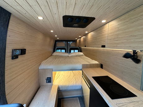 Modern RV rental interior with a cozy bed, sleek kitchen, and light wood paneling, perfect for adventure.
