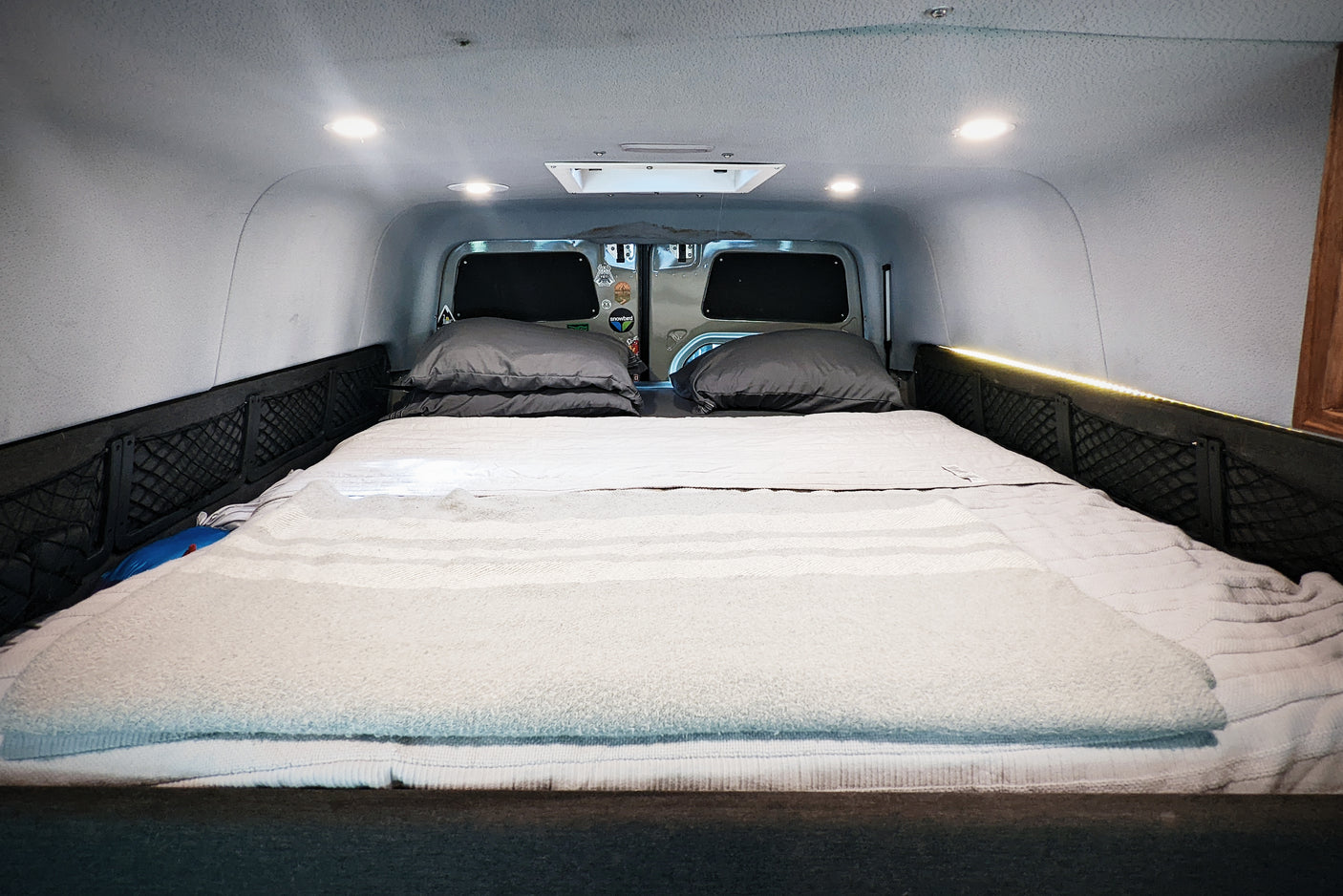 Cozy rv rental interior featuring a comfortable bed with soft bedding, overhead lights, and practical side storage nets.