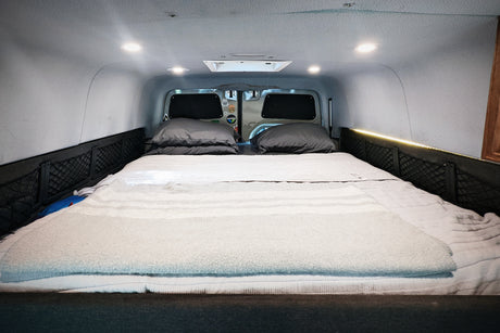 Cozy rv rental interior featuring a comfortable bed with soft bedding, overhead lights, and practical side storage nets.