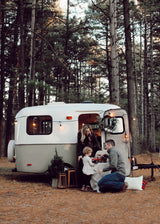 A family enjoys outdoor memories with their charming RV rental, nestled among towering pine trees.