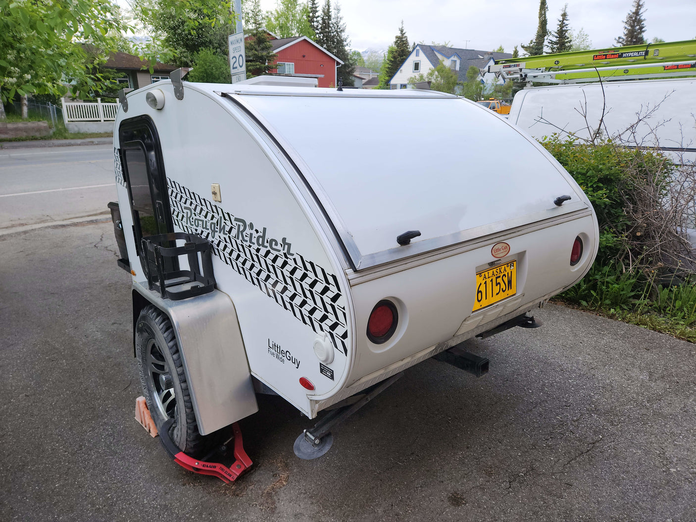 A white LittleGuy Rough Rider teardrop camper, perfect for an RV rental, with an Alaska license plate. Secured by a tire claw.