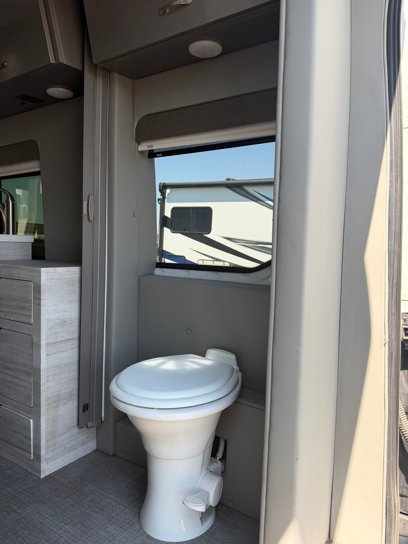  this white rv rental camper van features a roof rack and tinted windows. Driver's door open on sunny day.|Inside an RV rental: A white toilet sits in a compact gray interior — photo 2