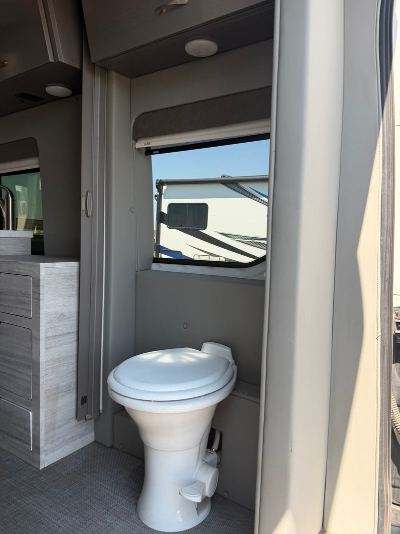 this white rv rental camper van features a roof rack and tinted windows. Driver's door open on sunny day.|Inside an RV rental: A white toilet sits in a compact gray interior — photo 2