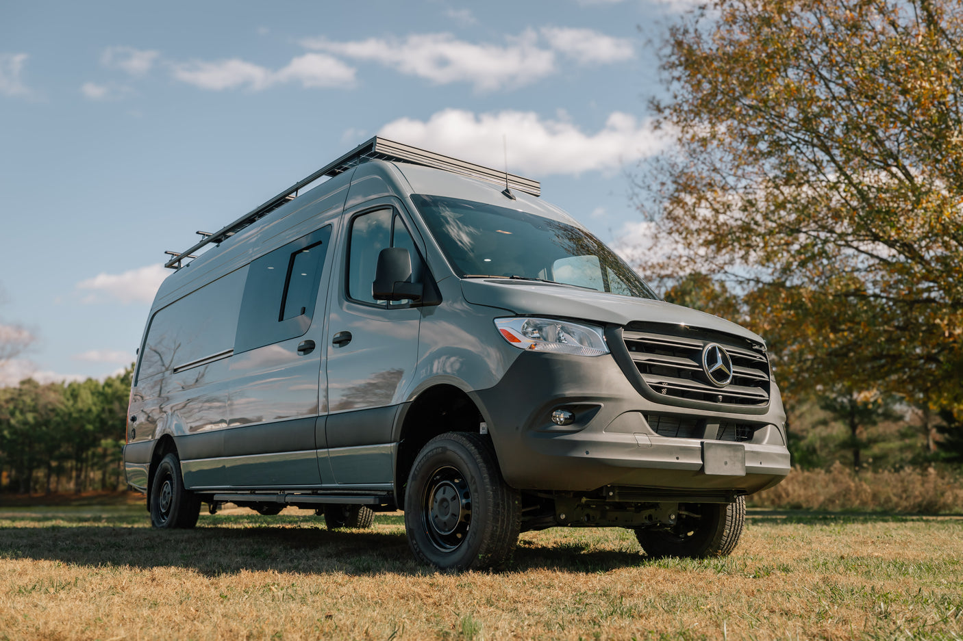 A gray Mercedes-Benz Sprinter camper van, ideal for an rv rental, parked in a grassy field under a blue sky.
