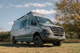 A gray Mercedes-Benz Sprinter camper van, ideal for an rv rental, parked in a grassy field under a blue sky.