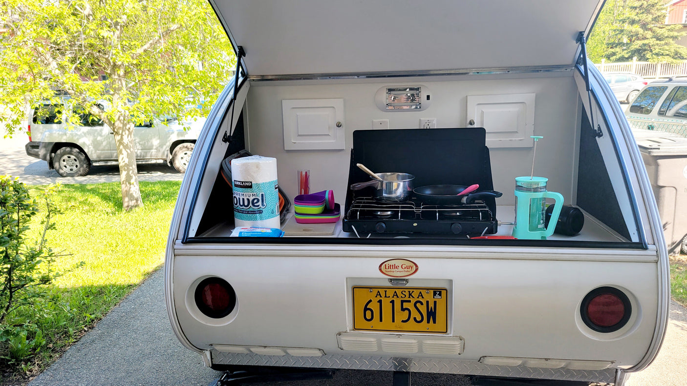 Compact rv rental teardrop camper features a fully equipped outdoor kitchen with stove, pots, and camping essentials.