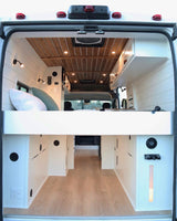 Spacious & modern camper van interior, viewed from the rear, featuring an elevated bed & ample storage. Ideal for RV rental.