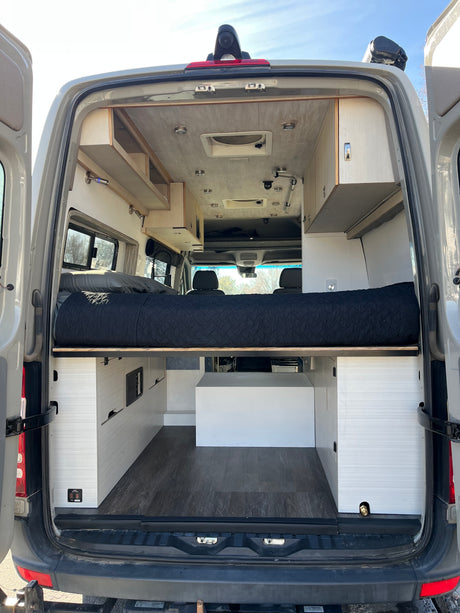 Rear view of an rv rental camper van's custom interior, featuring an elevated bed, storage, and ceiling lights.