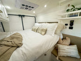 RV rental interior: A bright bedroom with white shiplap walls, soft bedding, built-in shelf, and controls.