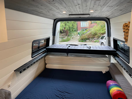 This RV rental features a cozy camper van interior with a bed, foldable platform, and wood-paneled ceiling.